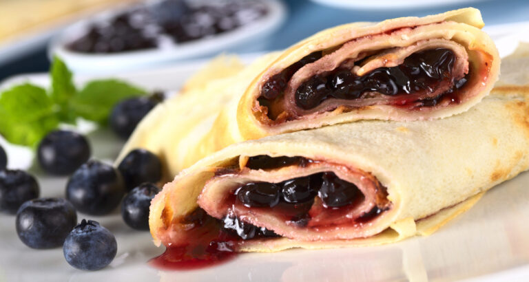 Kuvassa sinisiä marjoja, mustikoita, sekä vaaleita kääreitä, lettuja, joiden sisällä on mustikoita.